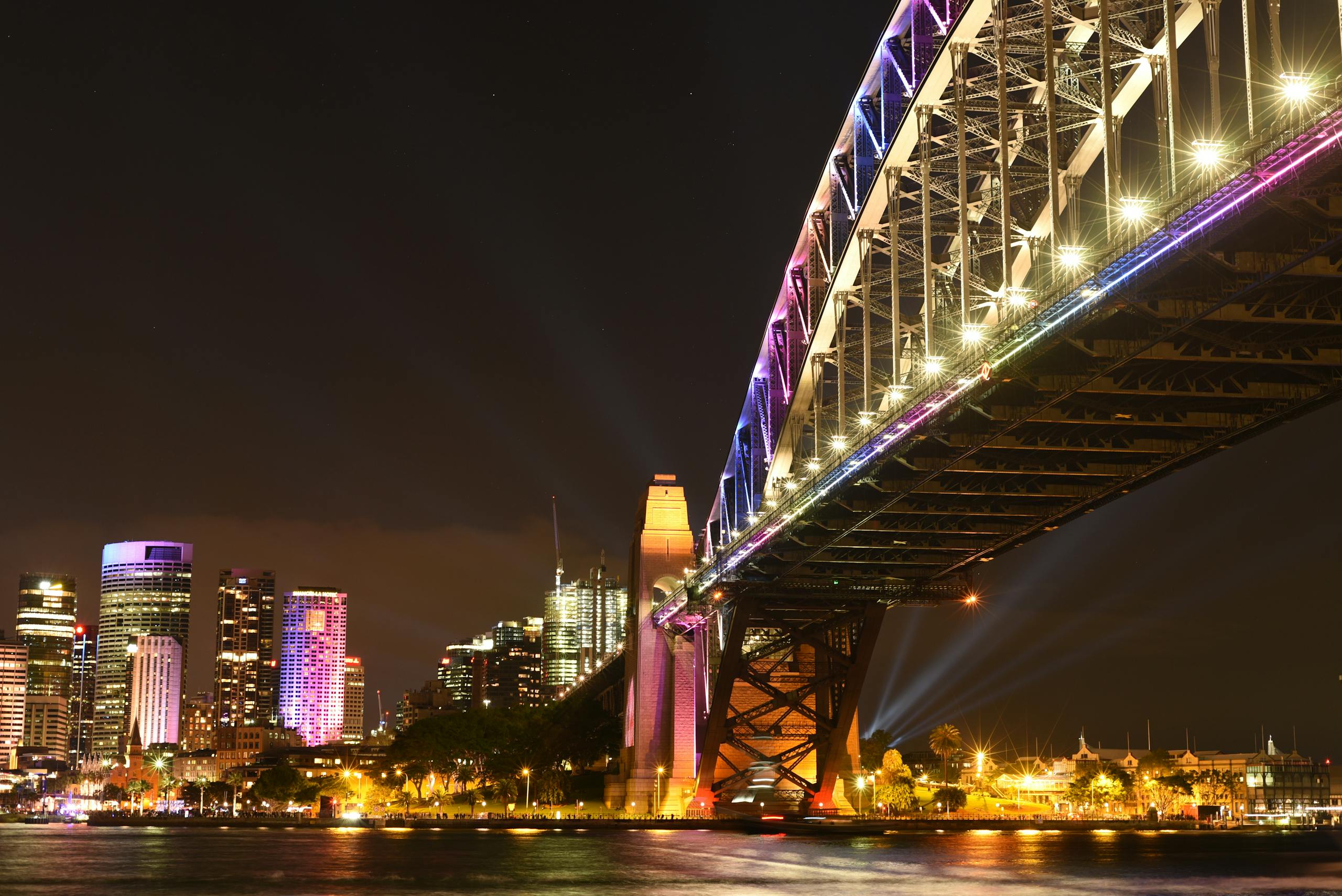 Stunning night view of Sydney Harbour Bridge with illuminated city skyline reflecting on the water.